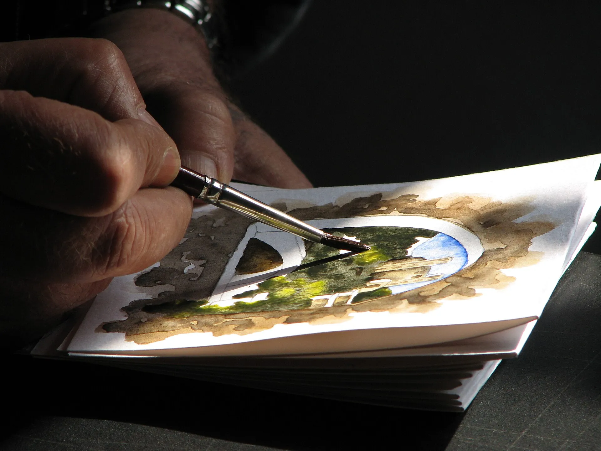 Un artiste peint une aquarelle en plein air, pinceau et palette à la main