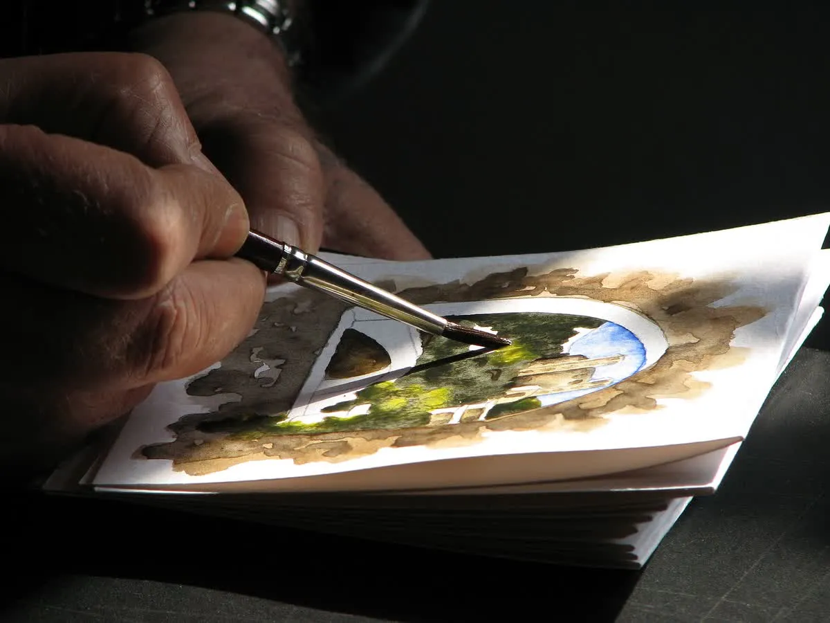 Un artiste peint une aquarelle en plein air, pinceau et palette à la main